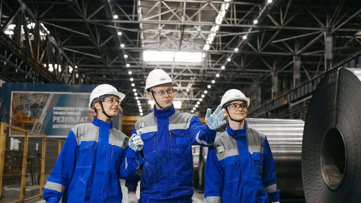 Industrial workers in safety gear walking through a steel factory
