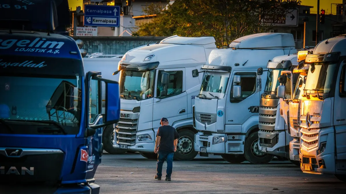 Commercial semi trucks parked at a freight terminal at sunset with a driver walking between them
